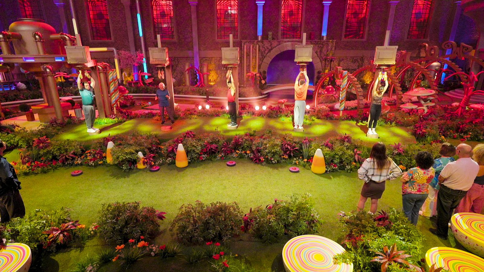 Contestants holding on to overhead handles during a challenge in the candy garden, Nick Spinelli on the far left in a teal shirt